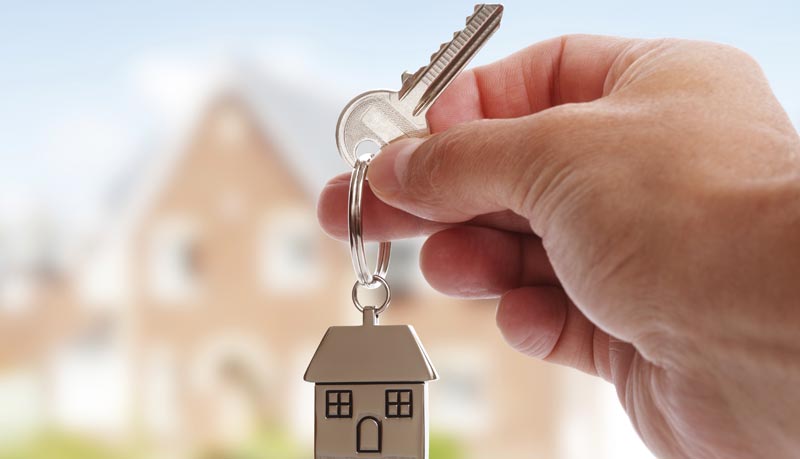 photo of hand holding key to house with house in background